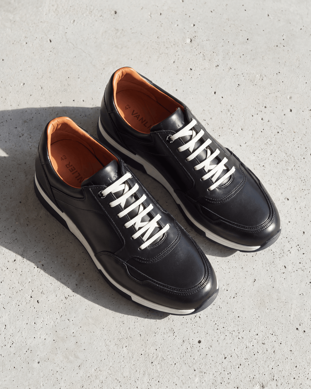 Zwart gladleren Positano sneaker – close-up van het paar op beton