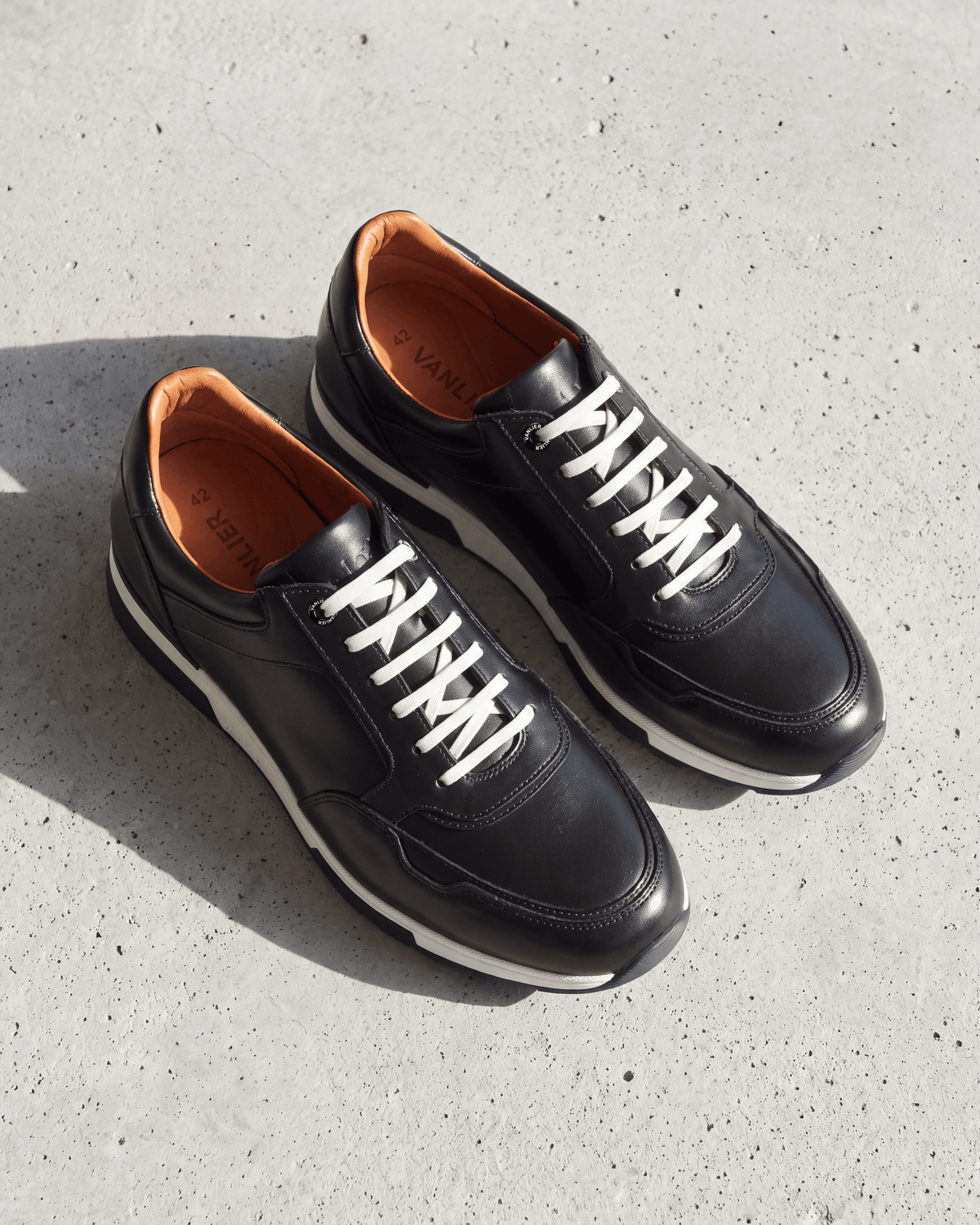 Zwart gladleren Positano sneaker – close-up van het paar op beton