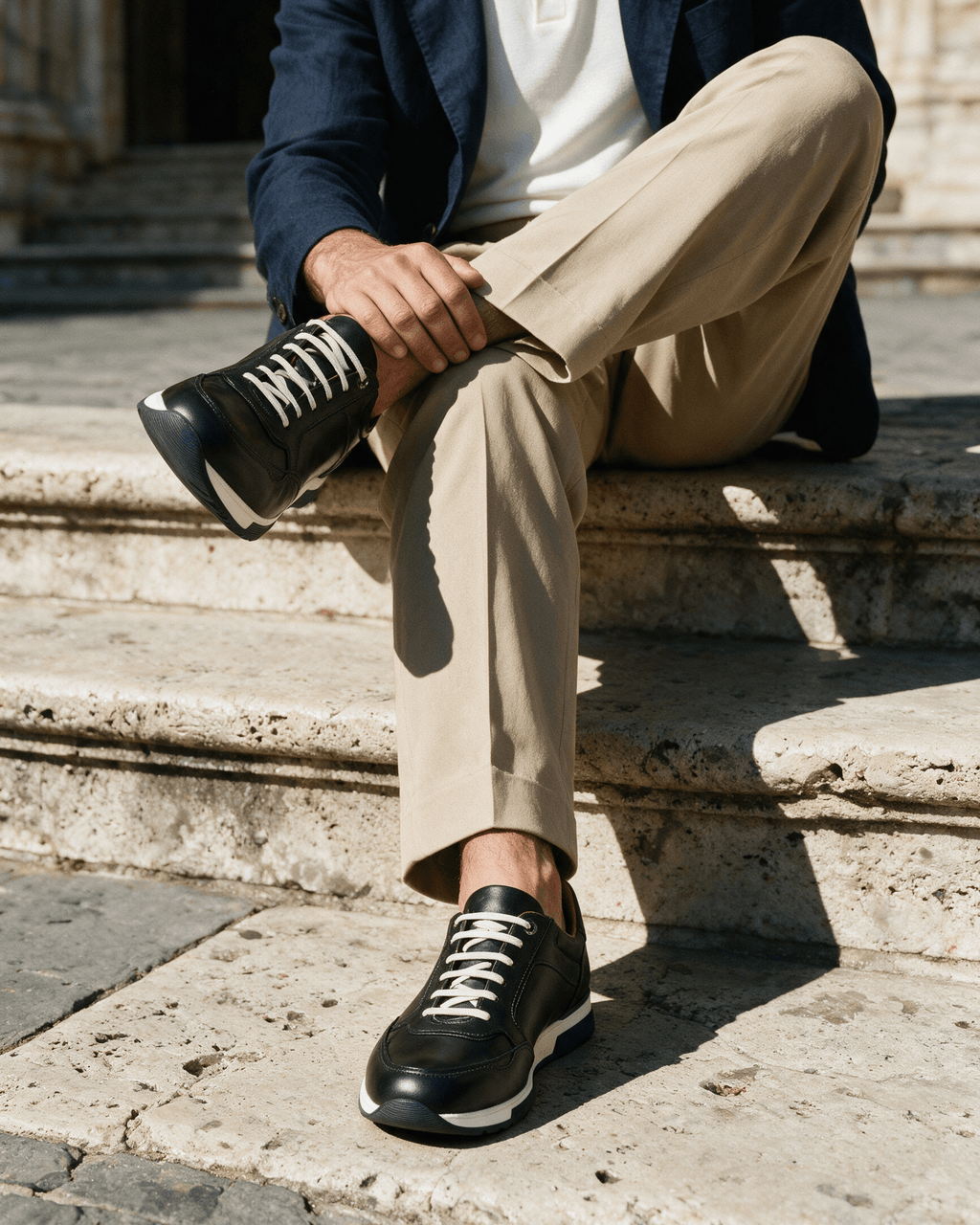 Zwart gladleren Positano sneaker – gedragen, zittend op een stenen trap