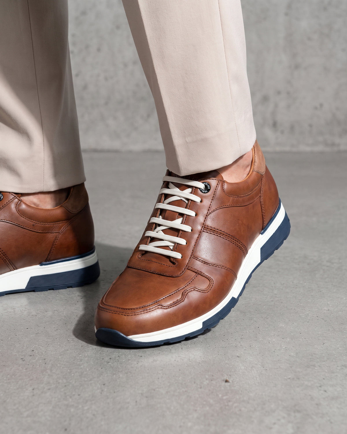 Cognac gladleren Positano sneaker – close-up van het paar in een betonnen atelier, andere hoek