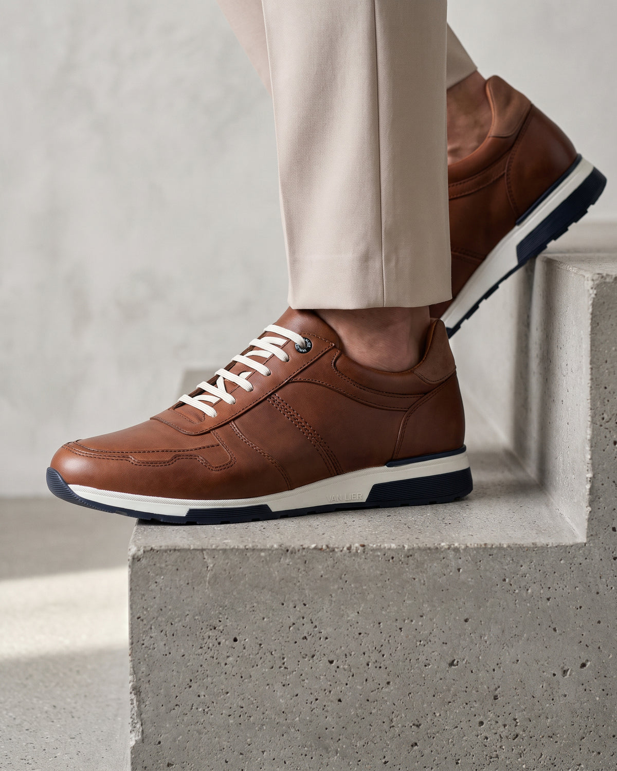 Cognac gladleren Positano sneaker – close-up van het paar in een betonnen atelier, derde opname