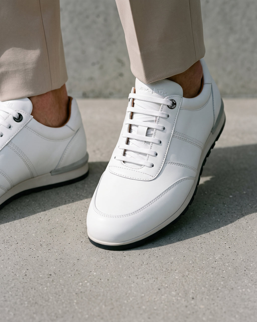Wit gladleren Anzano sneaker – close-up van het paar op een ruwe betonnen vloer