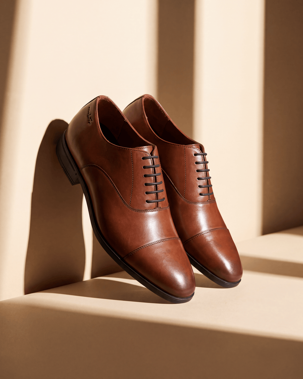 Cognac gladleren Portofino veterschoen – detail bij een raam met schaduw
