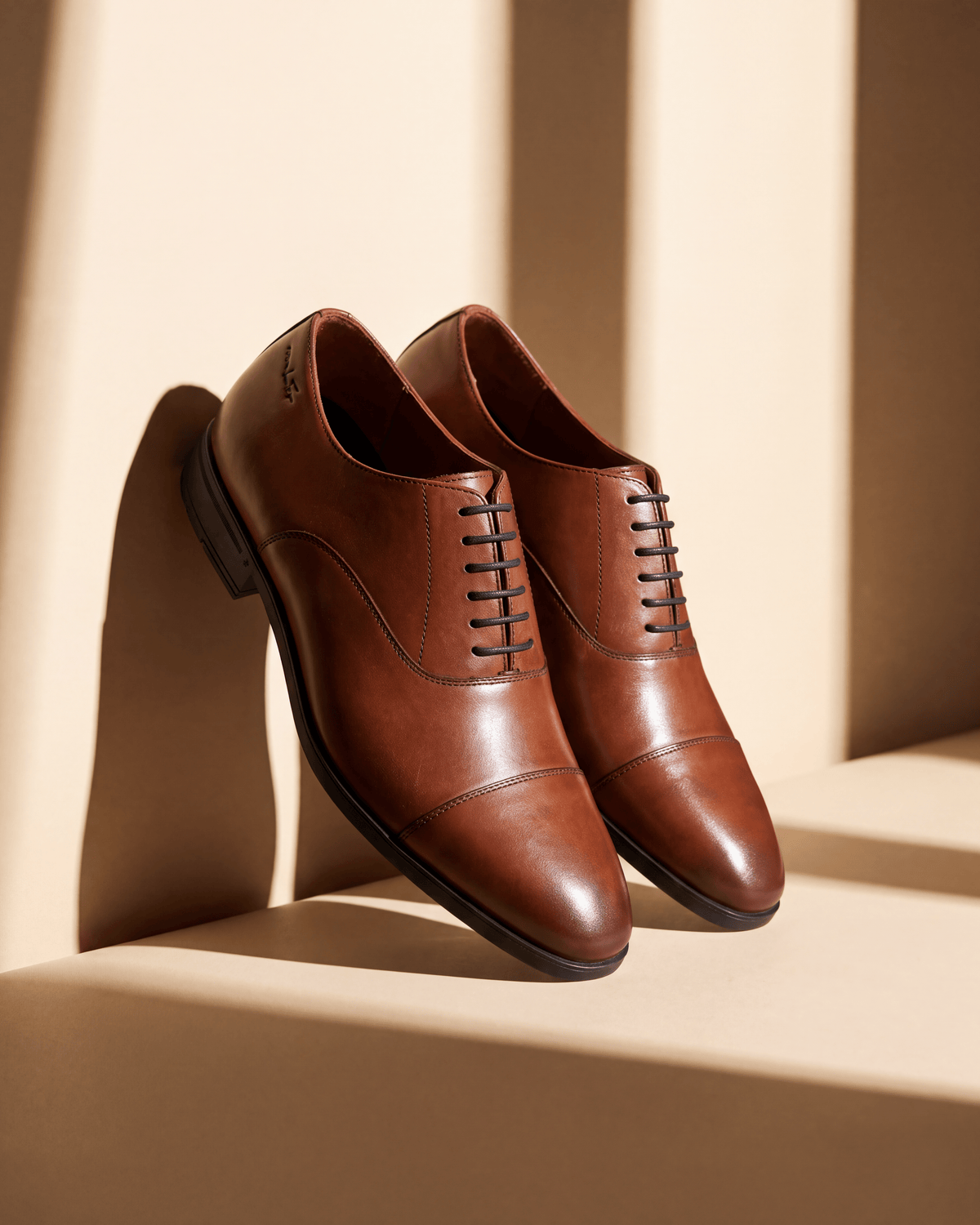 Cognac gladleren Portofino veterschoen – detail bij een raam met schaduw