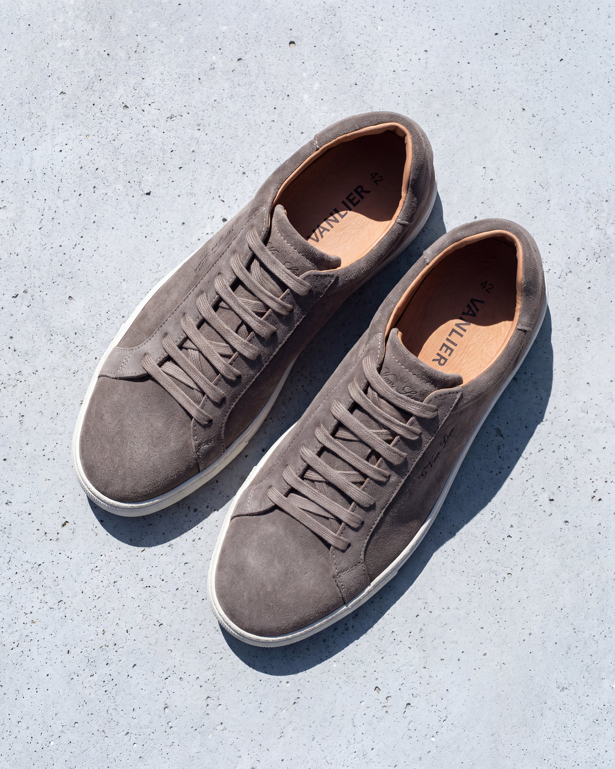 Taupe suède Napoli sneaker – close-up van het paar op ruw beton, andere hoek