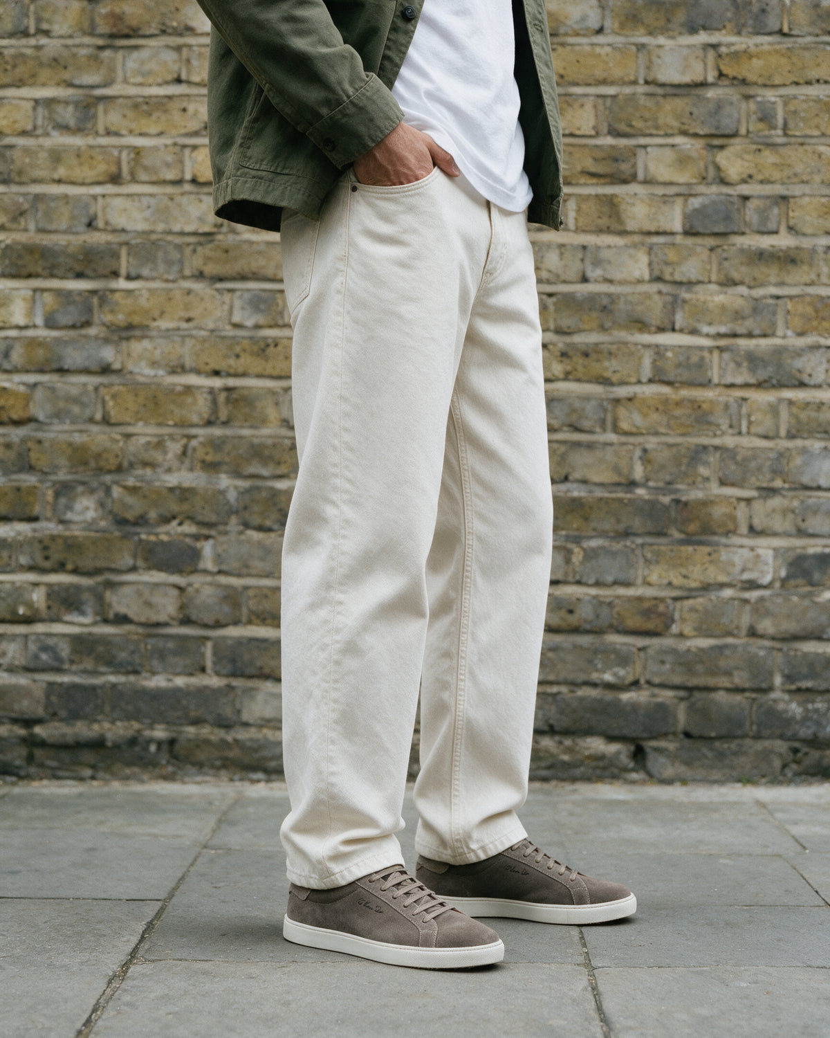 Taupe suède Napoli sneaker – lifestyle in profiel tegen een bakstenen muur