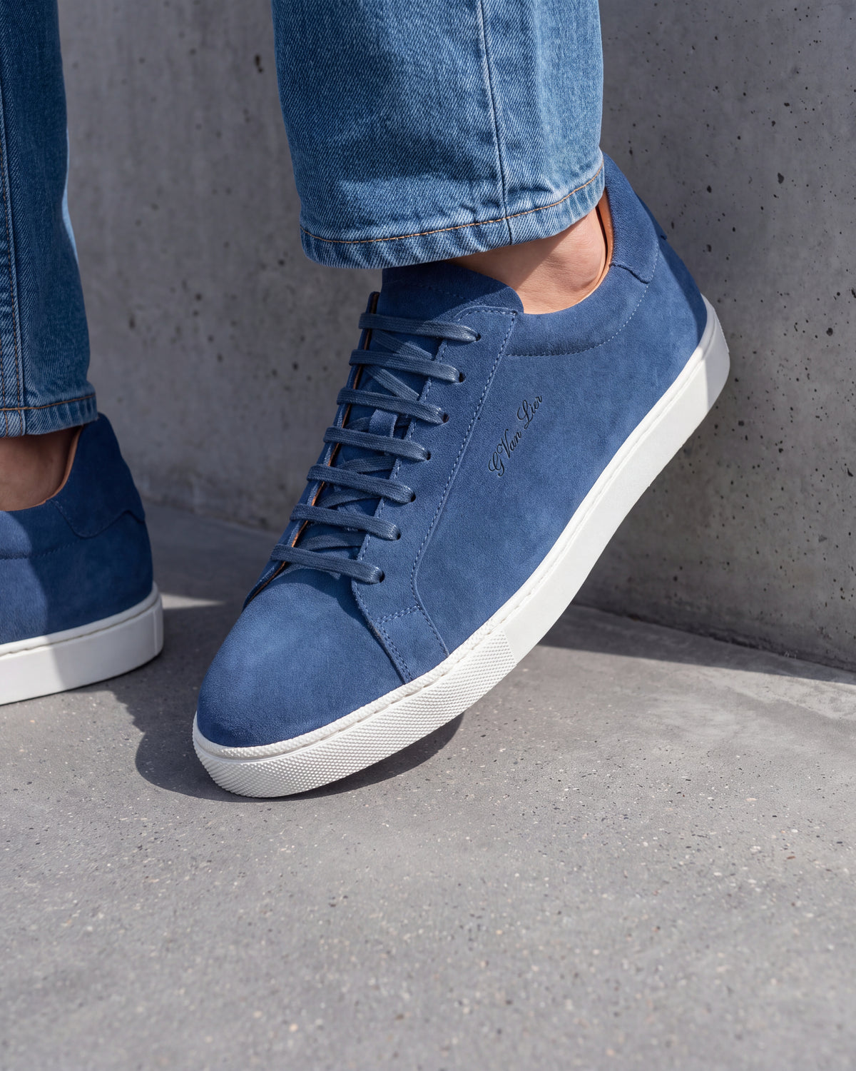 Blauw suède Napoli sneaker – close-up van het paar op een ruwe betonnen vloer, andere hoek