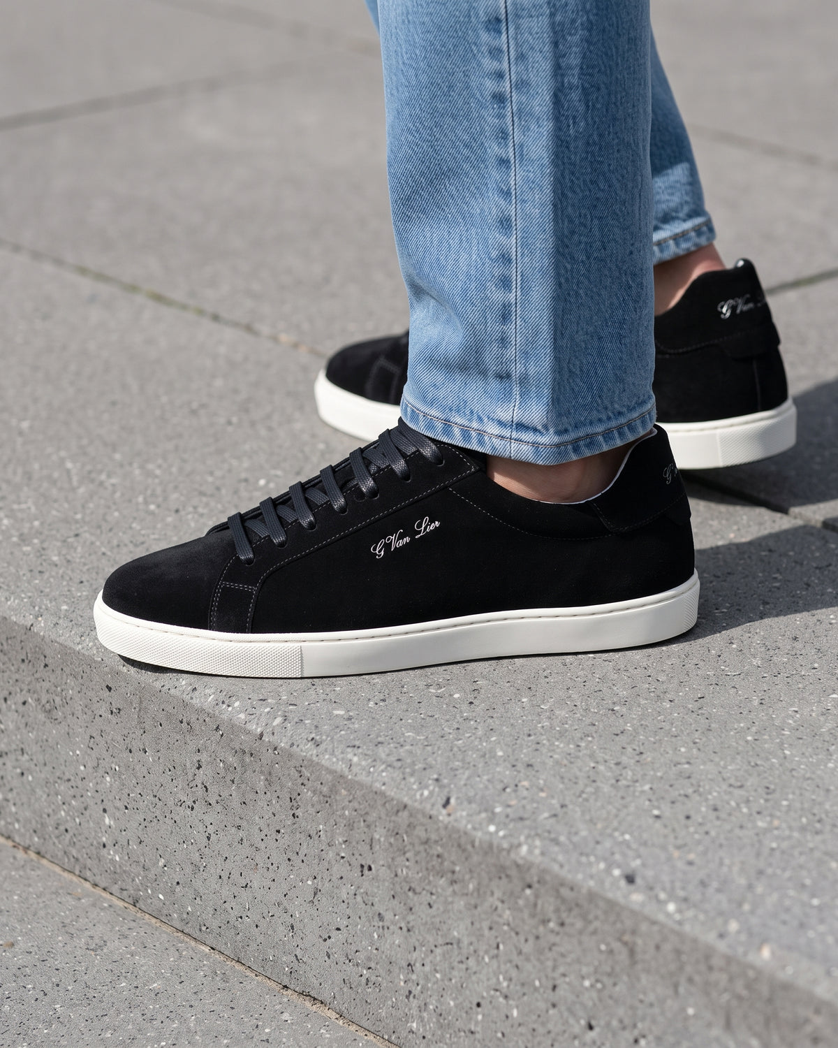 Zwart suède Napoli sneaker – close-up van het paar op een ruwe betonnen vloer