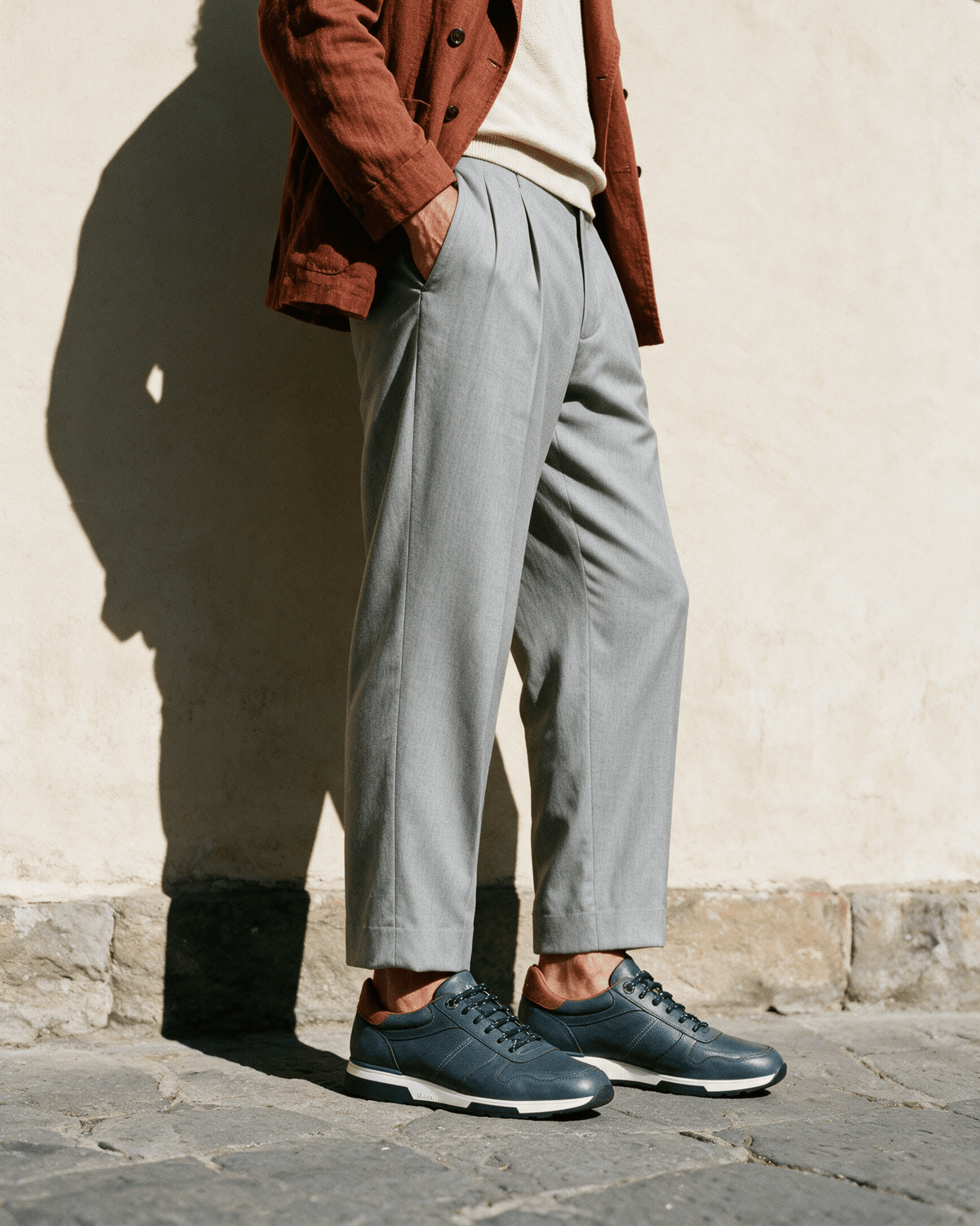 Navy blauw gladleren Positano sneaker – gedragen, in profiel tegen een crèmekleurige muur