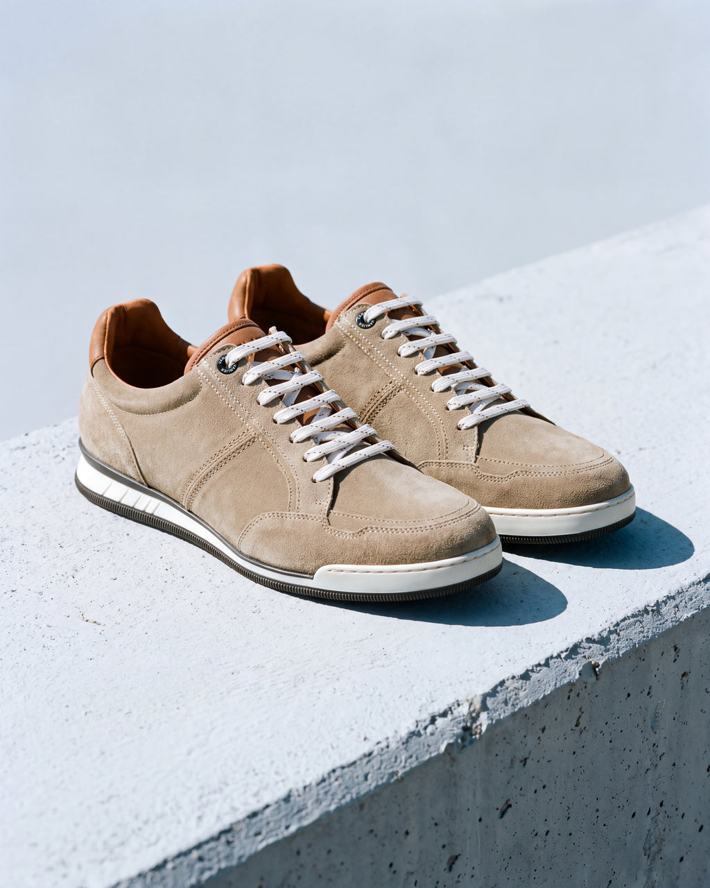 Zand beige suède Magnus sneaker – detail van het paar op ruw beton