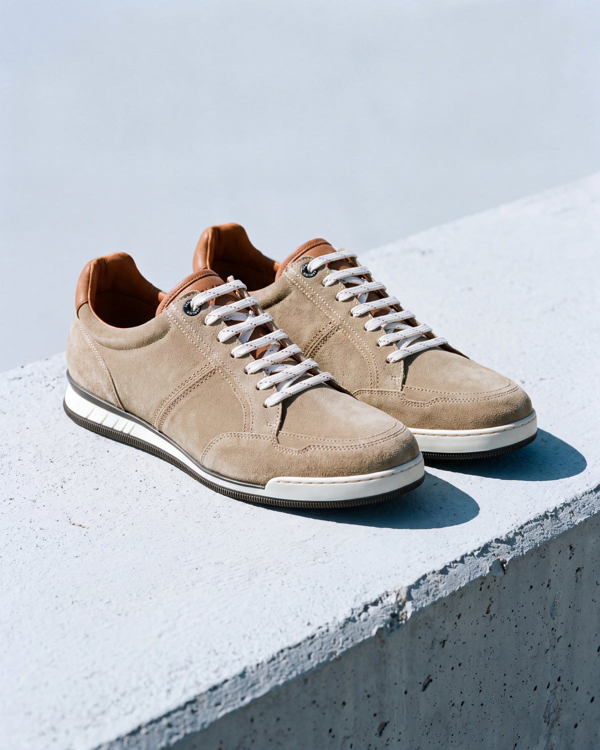 Zand beige suède Magnus sneaker – detail van het paar op ruw beton