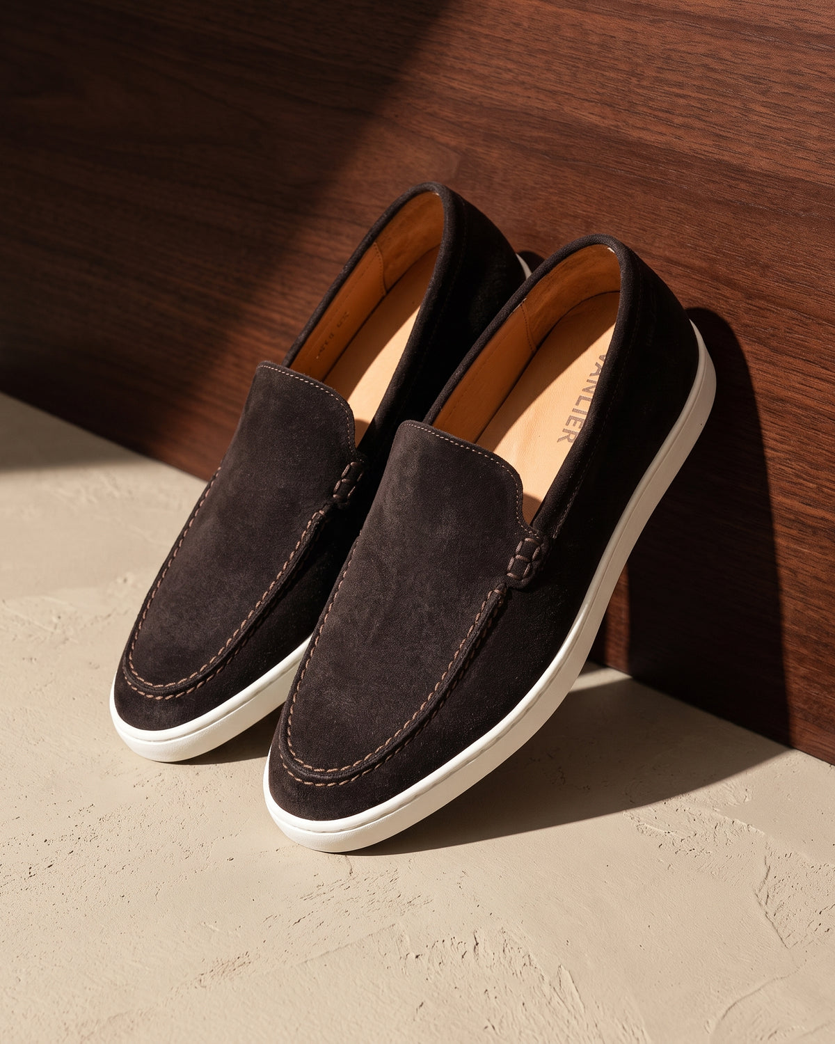 Testa di moro bruin suède Lugano loafer – detail van het paar op hout en pleisterwerk