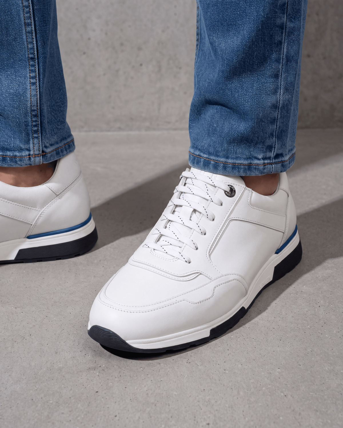 Wit gladleren Positano sneaker – close-up van het paar op ruw beton