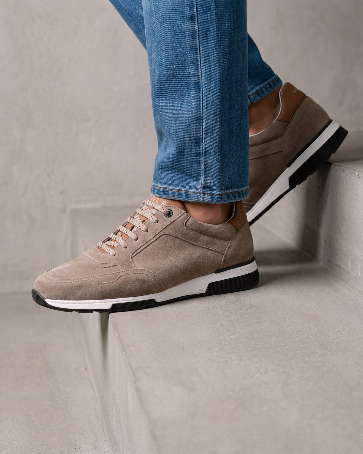 Taupe suède Positano sneaker – close-up van het paar op beton in een atelier