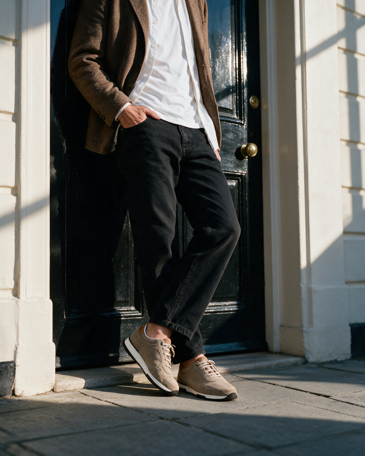 Taupe suède Positano sneaker – lifestyle tegen een zwarte deur geleund