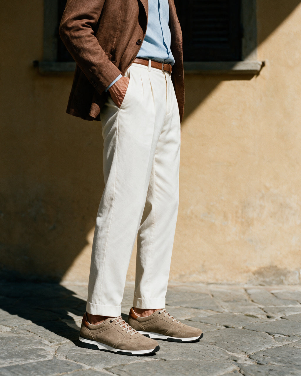 Taupe suède Positano sneaker – lifestyle in profiel bij een okerkleurige muur