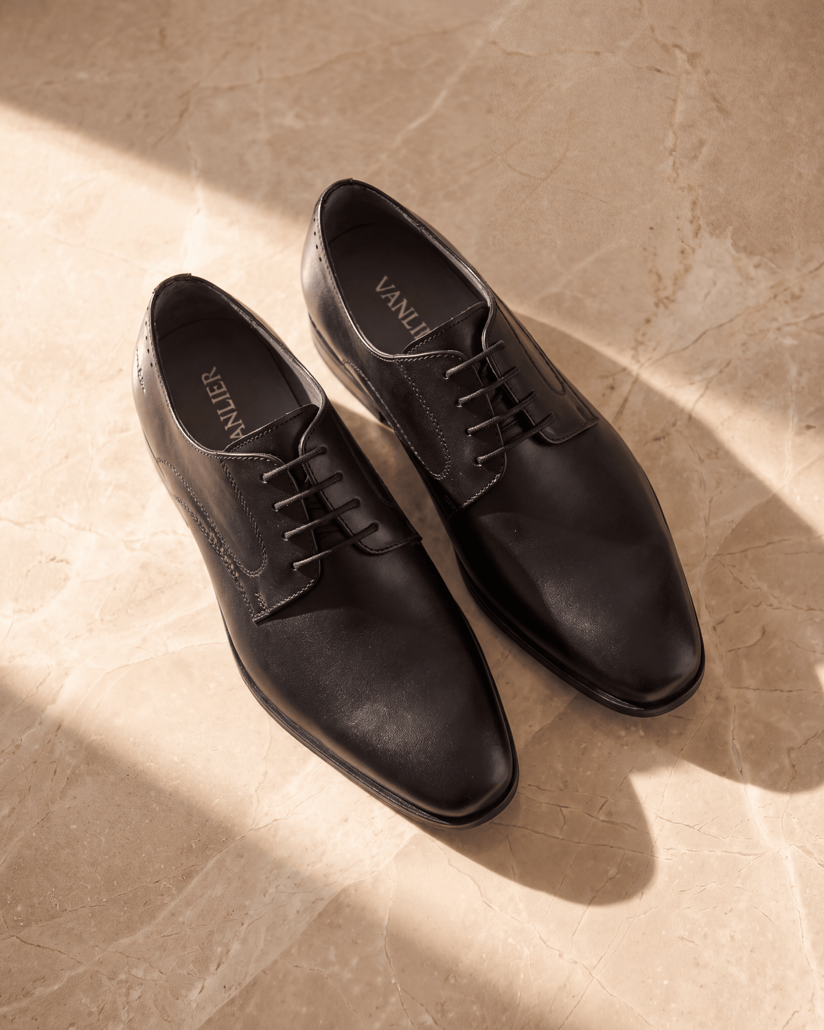 Zwart gladleren met rubberen zool Rhodes veterschoen – het paar op warm marmer