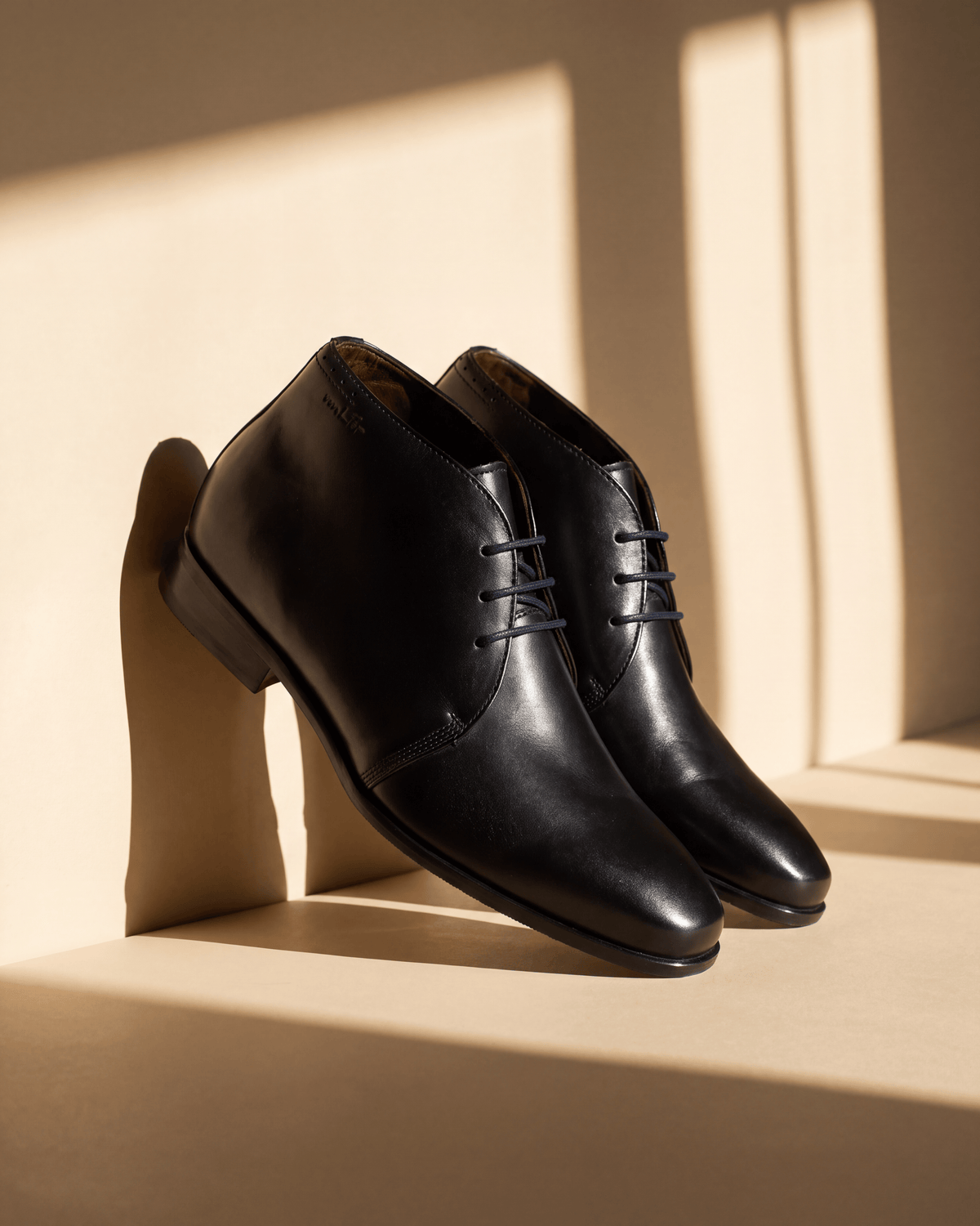 Zwart gladleren met rubberen zool Rhodes halfhoge veterschoen – het paar op een vloer met raamschaduw