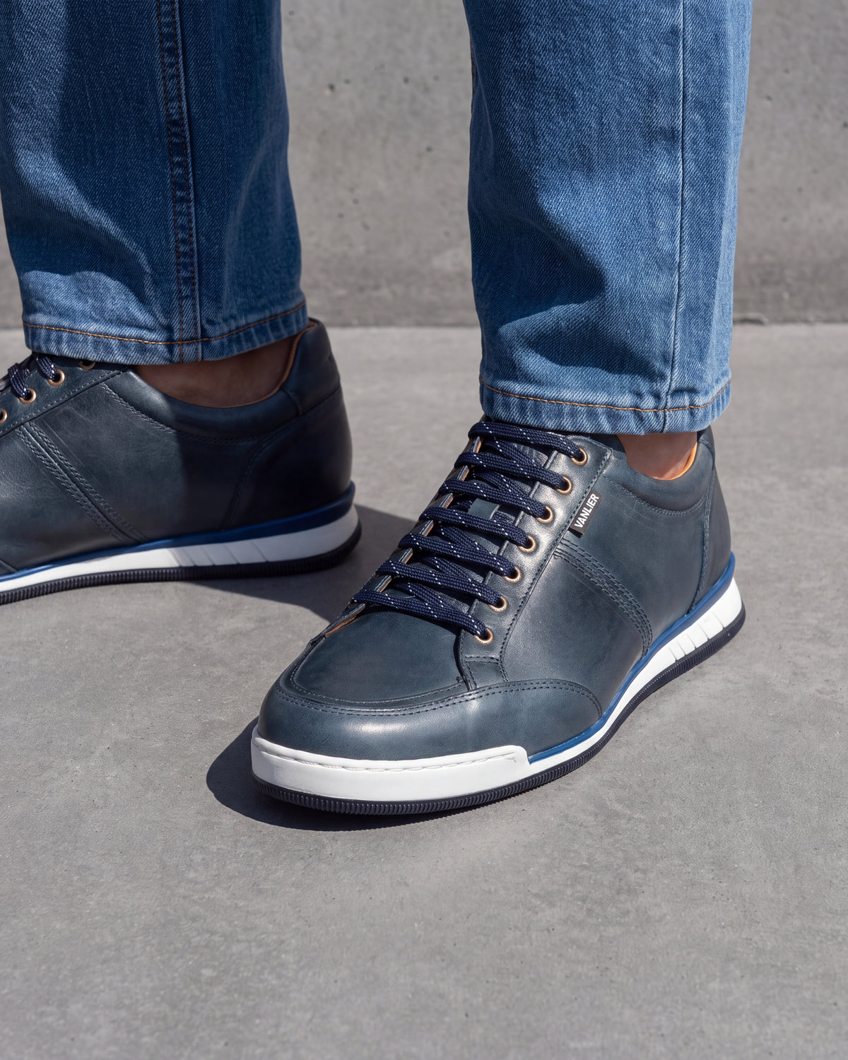 Blauw gladleren Magnus sneaker – close-up van het paar op een ruwe betonnen vloer