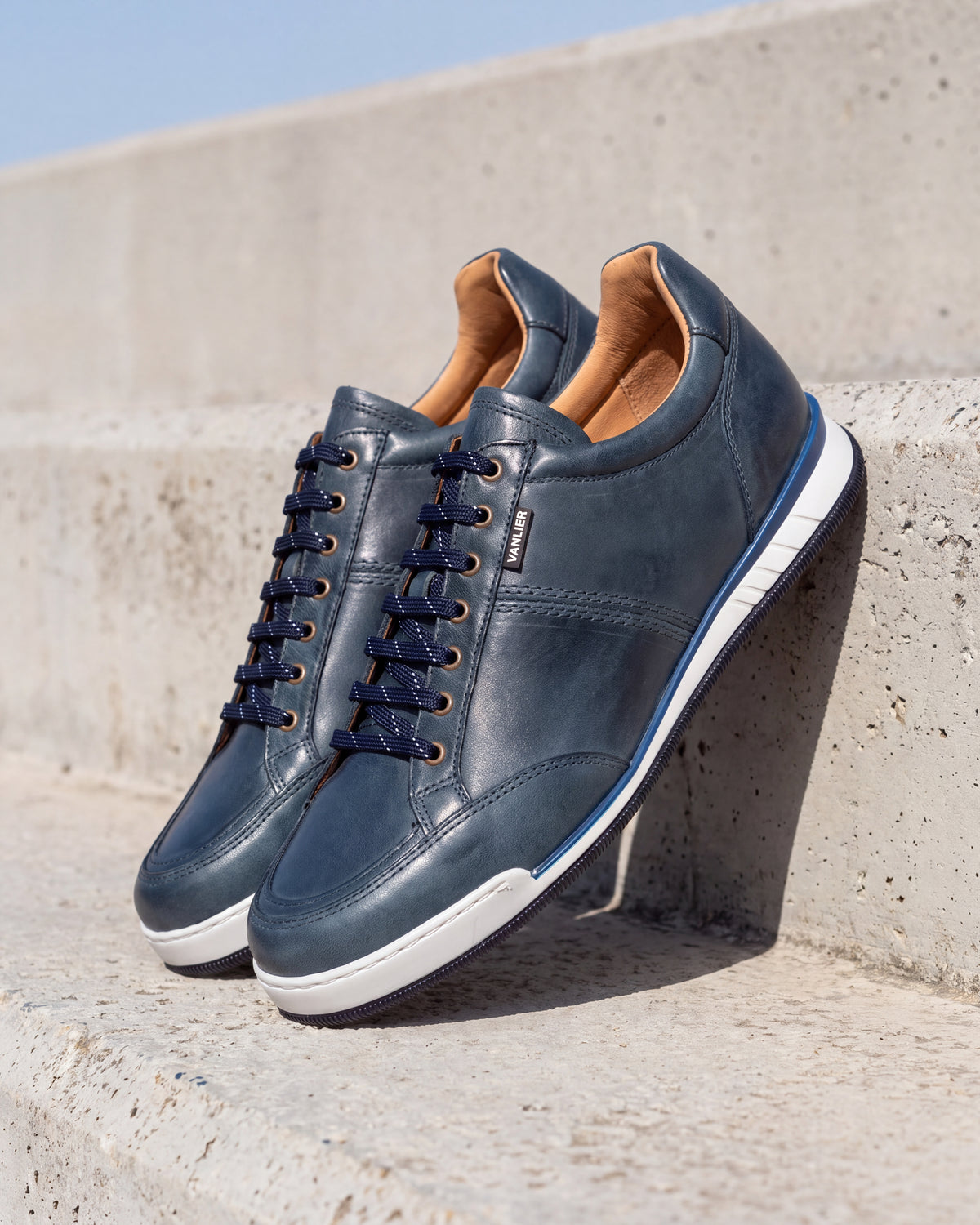 Blauw gladleren Magnus sneaker – paar op ruw beton, andere hoek