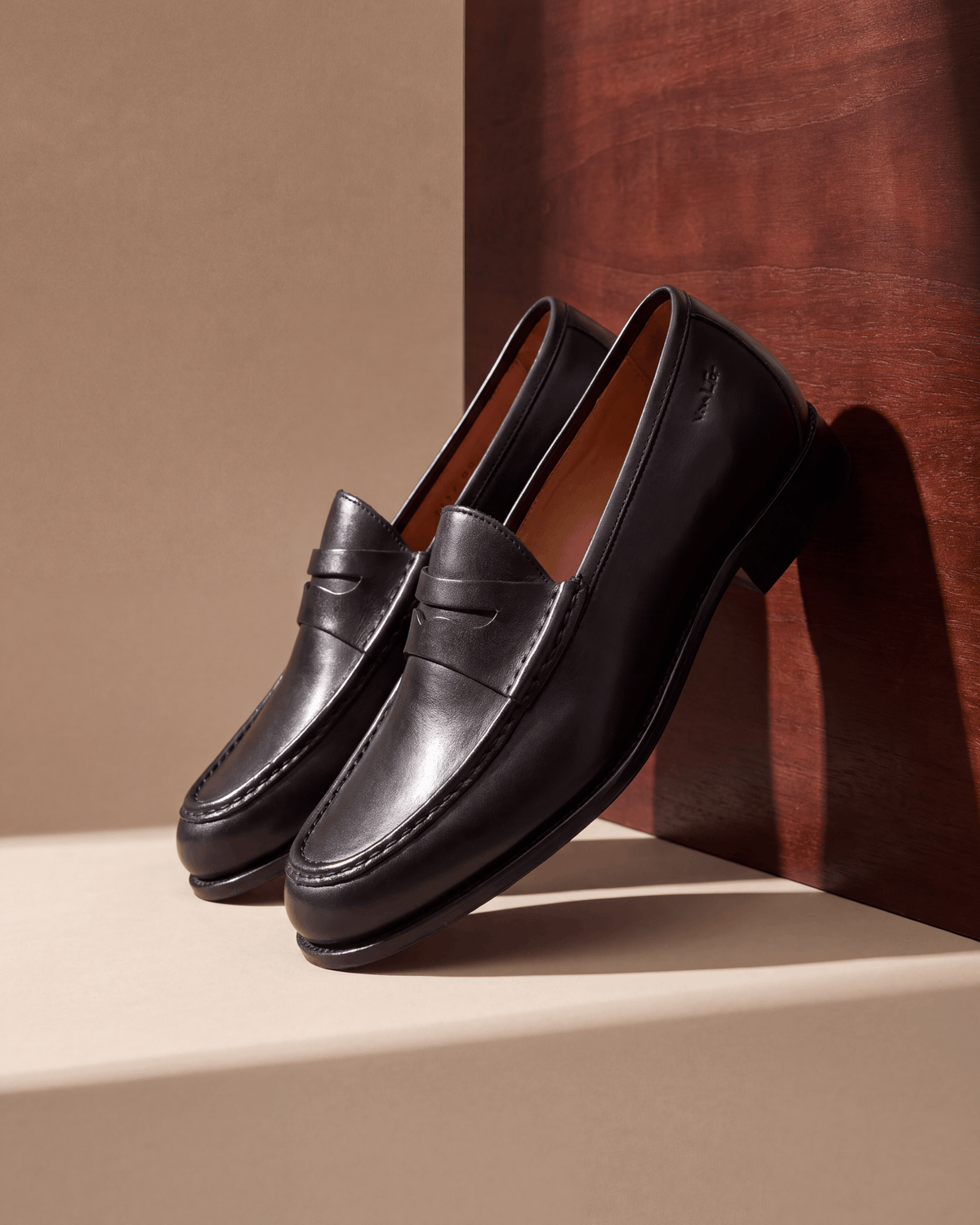 Zwart gladleren Cambridge Penny loafer – close-up van het paar tegen een muur